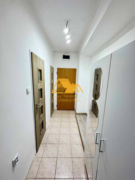 Chodba s bílými stěnami, dlažbou a dřevěnými dveřmi v 3-pokojovém bytě.