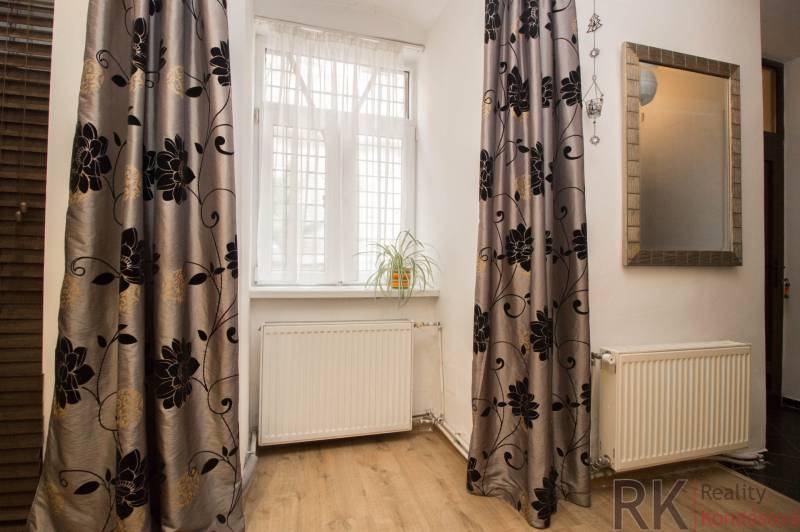 Pokoj v 2-pokojovém bytě s podlahou s dřevěným dekorem, závěsy a květinou na parapetu.