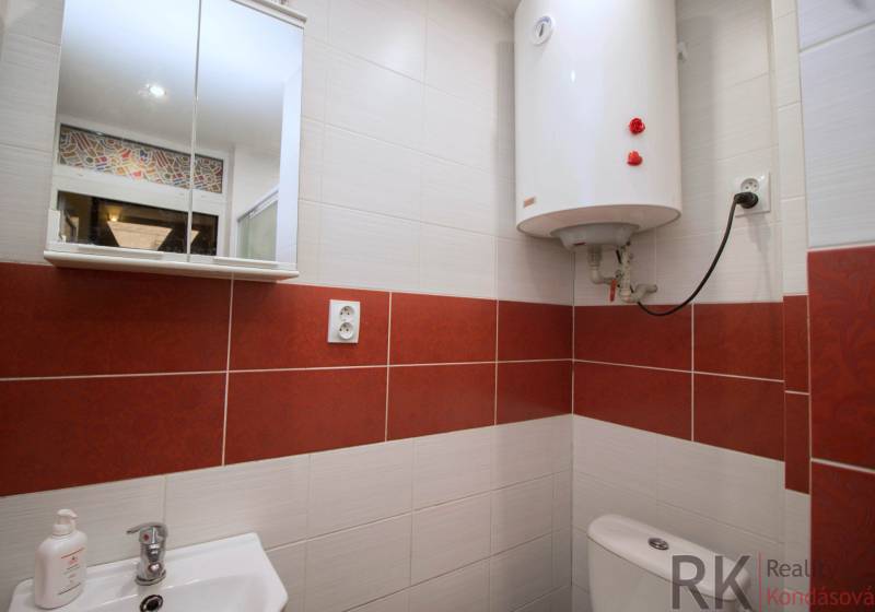 Koupelna s bílým bojlerem, umyvadlem a zrcadlovou skříňkou ve 2-pokojovém bytě.