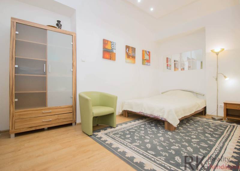 Ložnice v 2pokojovém bytě s podlahou s dřevěným dekorem, kobercem a postelí.