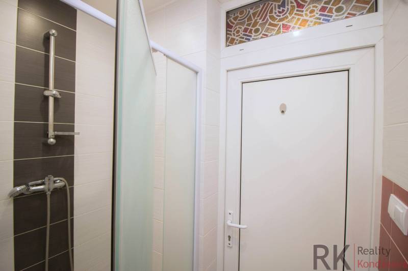 Koupelna s kombinací bílých a tmavých obkladů v 2-pokojovém bytě.