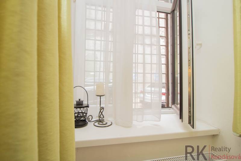 Otevřené okno v 2-pokojovém bytě se závěsy a dekoracemi na parapetu.