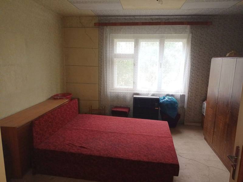 Ložnice v rodinném domě s jednoduchým nábytkem a červenou postelí.