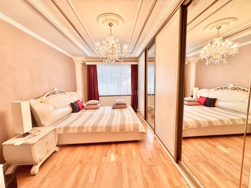 Ložnice s lustrem, velkou postelí a podlahou s dřevěným dekorem v 2-pokojovém bytě.