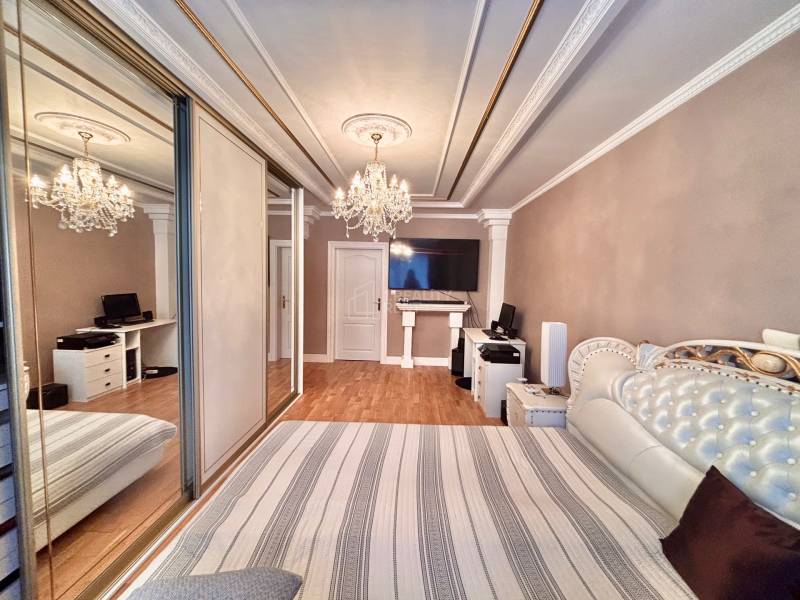 Ložnice v 2-pokojovém bytě s podlahou s dřevěným dekorem a velkou zrcadlovou skříní.