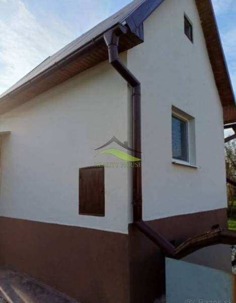 Chata v Pozdišovcích s bílou fasádou a tmavým okapovým systémem.