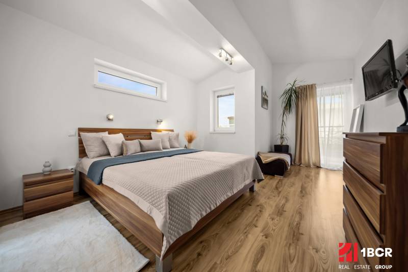 Ložnice v rodinném domě s postelí, dekorativními prvky a podlahou s dřevěným dekorem.