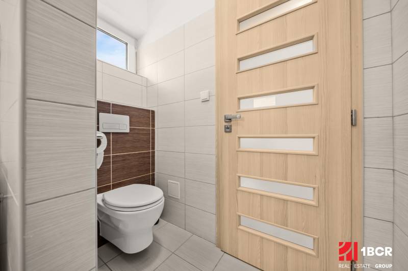 Toaleta v rodinném domě se světlými obklady a dveřmi s vertikálními pruhy.