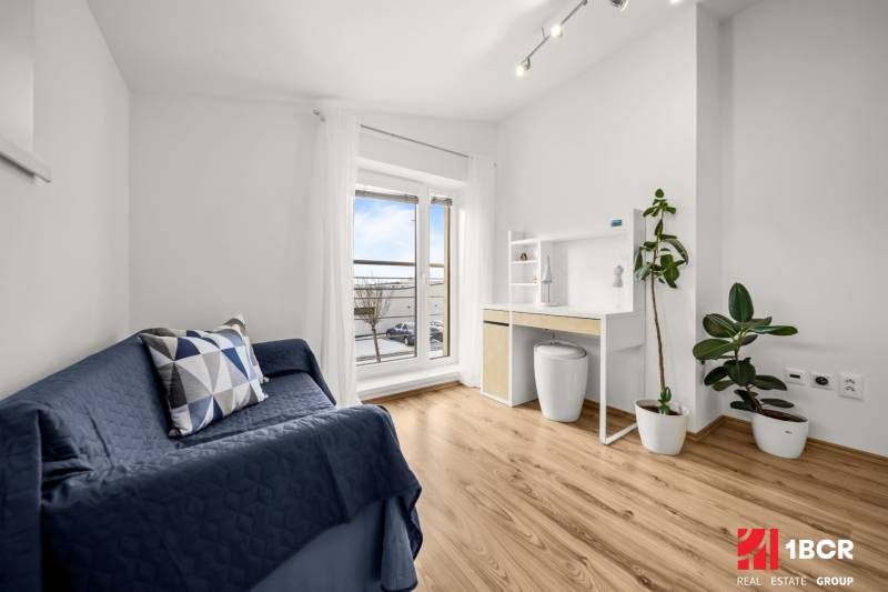 Pokoj v rodinném domě s podlahou s dřevěným dekorem, modrou pohovkou a pracovním stolem.