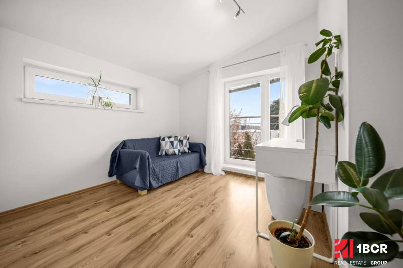 Pokoj v rodinném domě s pohovkou, okny a podlahou s dřevěným dekorem.