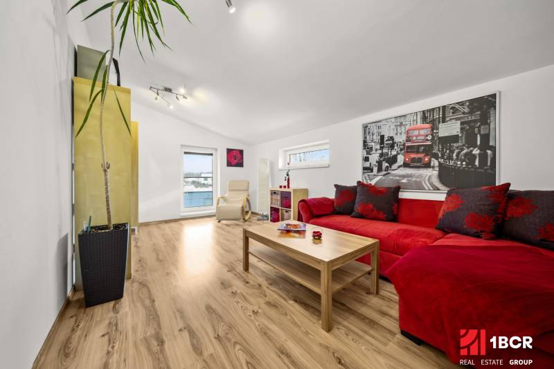 Obývací pokoj s podlahou s dřevěným dekorem, červenou sedačkou a velkou rostlinou.