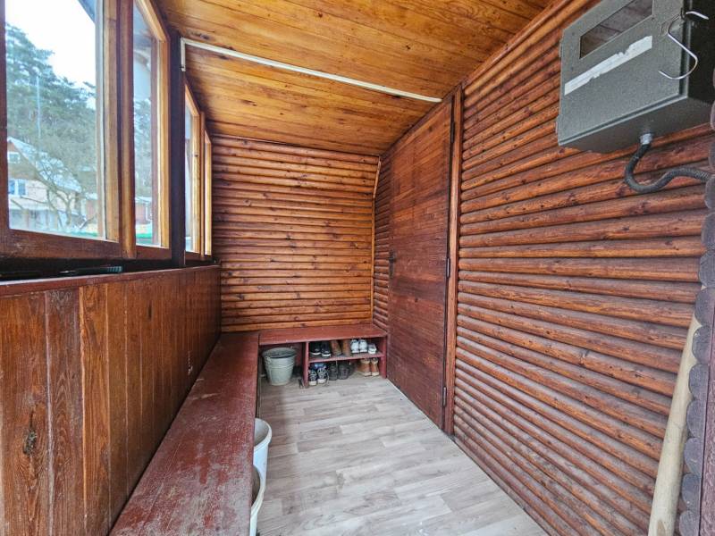 Dřevěná veranda chaty s podlahou s dřevěným dekorem a lavicí na uskladnění.