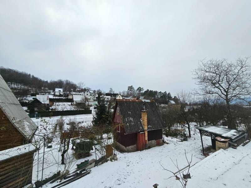 Zasněžená chata v Lieskovci v Dubnici nad Váhom obklopená stromy a dalšími chatami.