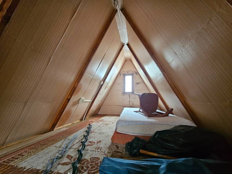 Podkroví chaty s matrací a židlí, dřevěný dekor, světlé stěny.