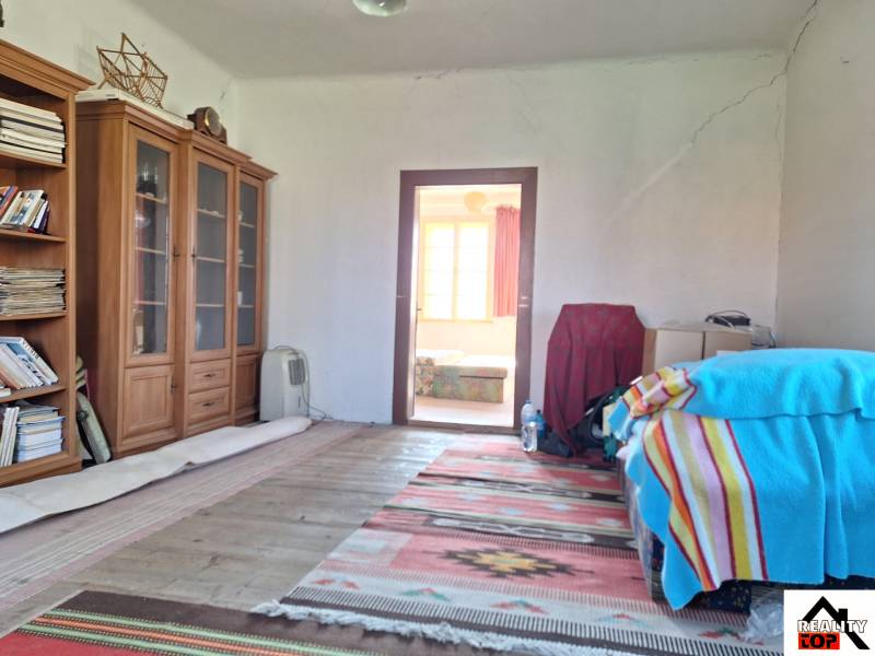 Pokoj v rodinném domě s regály na knihy, postelí s barevnou dekou a kobercem.