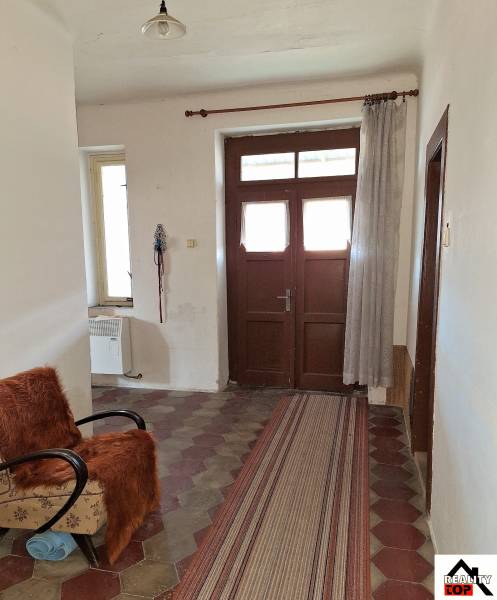 Chodba rodinného domu s dlaždicovou podlahou, křeslem a závěsem.