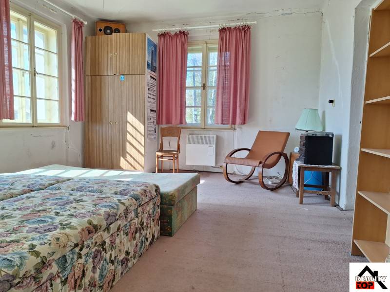 Pokoj s květinovou pohovkou, křeslem, skříní a růžovými závěsy v rodinném domě.