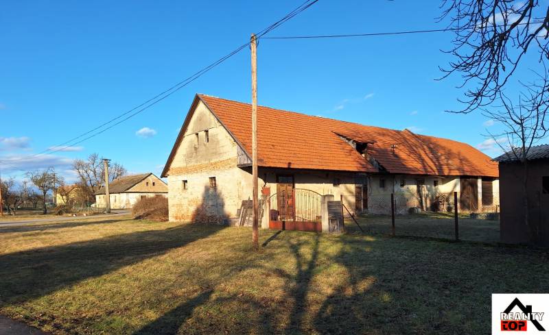 Kamenný rodinný dům v Orávce s červenou střechou obklopený travnatým pozemkem.