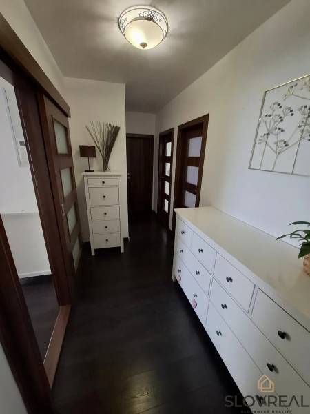 Chodba v 3-pokojovém bytě s tmavou podlahou a bílým nábytkem.