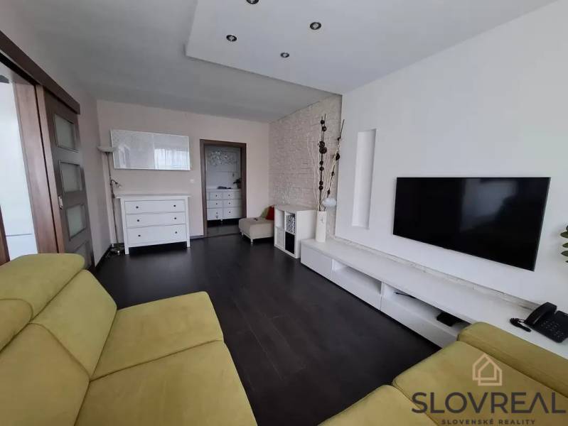 Obývací pokoj v 3pokojovém bytě s podlahou s dřevěným dekorem, TV a sedací soupravou.