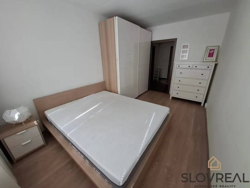 Ložnice v 3pokojovém bytě s podlahou s dřevěným dekorem, postelí a bílým nábytkem.