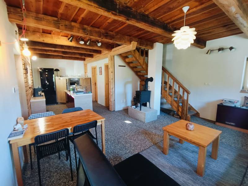 Interiér chaty s podlahou s dřevěným dekorem, dřevěným stropem a kachlovými kamny.