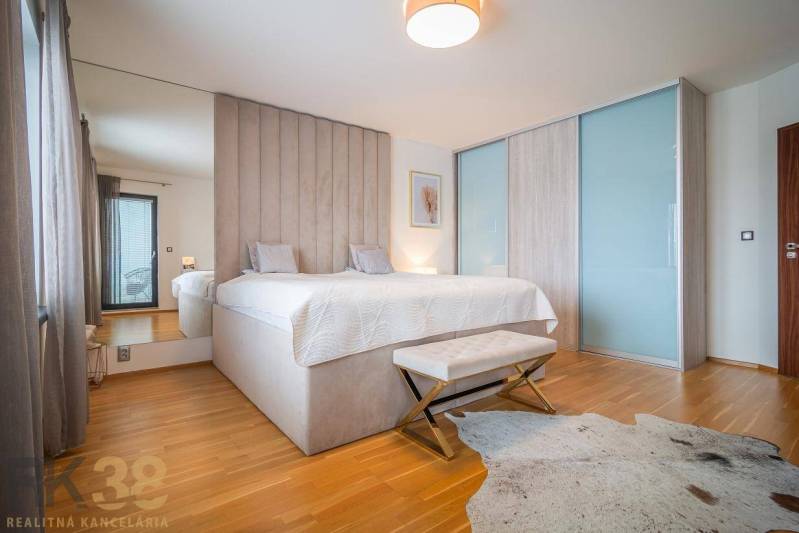 Ložnice v rodinném domě s postelí, podlahou s dřevěným dekorem a kožešinovým kobercem.