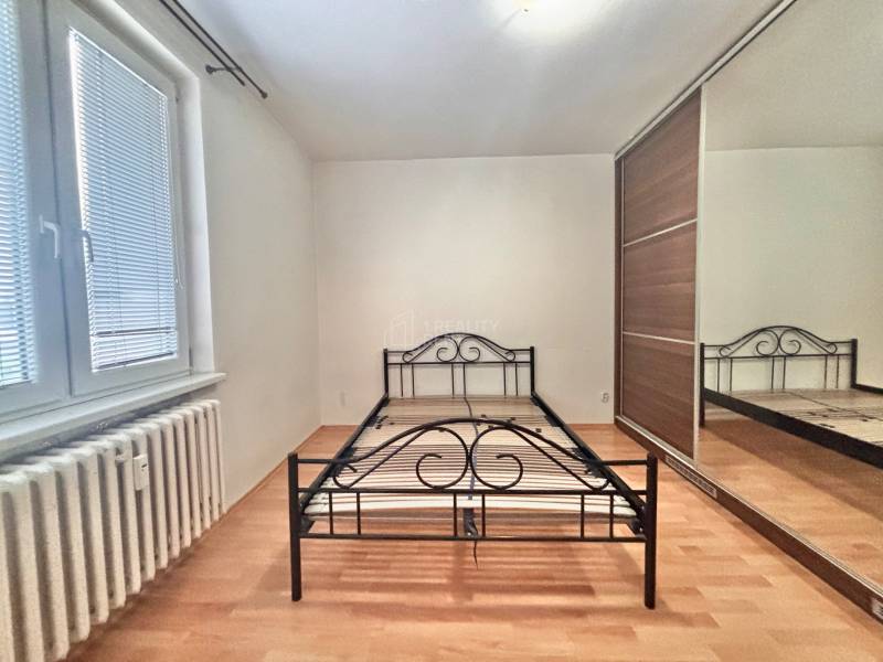 Ložnice s kovovou postelí, vestavěnou skříní a podlahou s dřevěným dekorem ve 3pokojovém bytě.