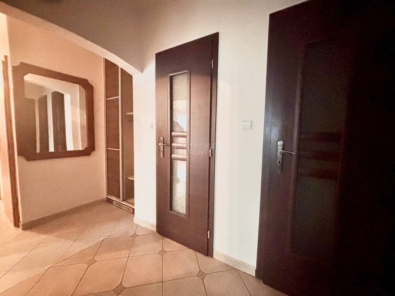 Chodba v 3-pokojovém bytě s dlažbou, zrcadlem a tmavými dveřmi.