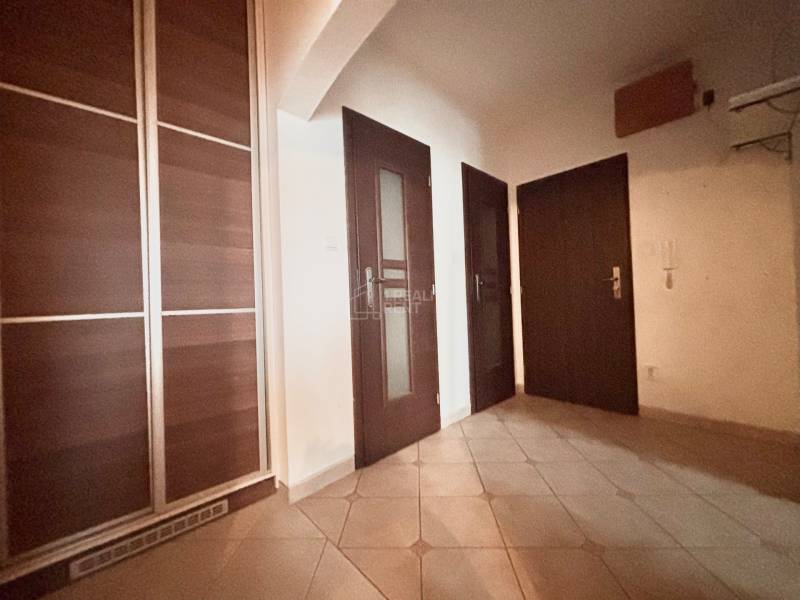 Chodba v 3-pokojovém bytě s tmavými dveřmi a vestavěnou skříní.