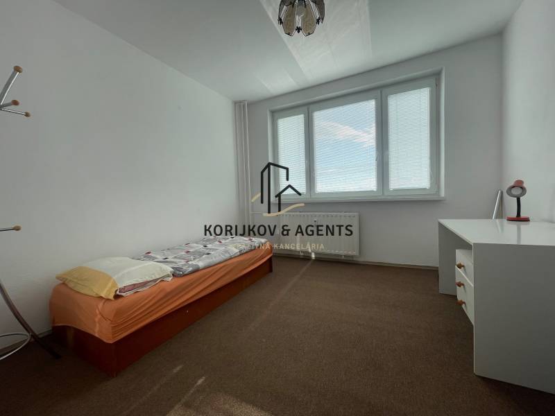 Jednoduchá ložnice s postelí, psacím stolem a kobercovým povrchem ve 3pokojovém bytě.