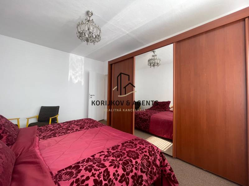 Ložnice s velkou skříní, lustrem a postelí v 3-pokojovém bytě.