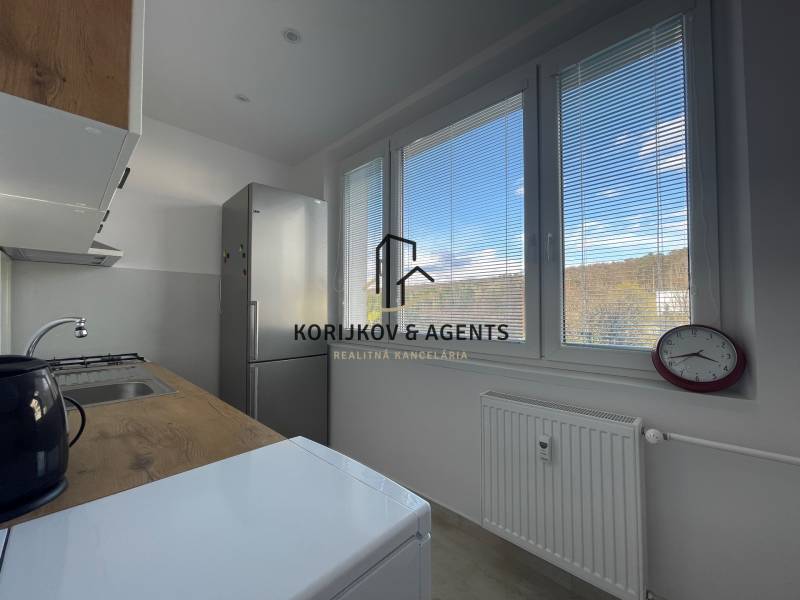 Kuchyně v 3-pokojovém bytě s výhledem přes žaluzie, jednoduché zařízení a spotřebiče.