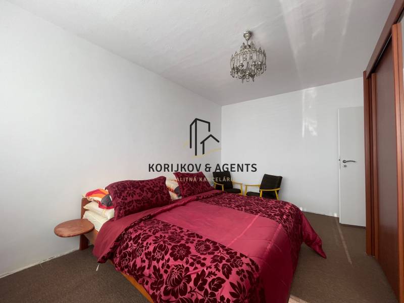 Ložnice s postelí s vzorovaným povlečením, stropním svítidlem a šatní skříní ve 3pokojovém bytě.