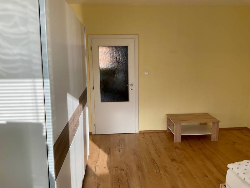 Pokoj s podlahou s dřevěným dekorem, světlými stěnami a jednoduchým nábytkem v 3-pokojovém bytě.