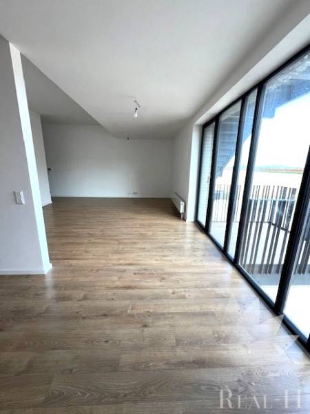 Obývací pokoj v 2-pokojovém bytě s podlahou s dřevěným dekorem a velkými okny.