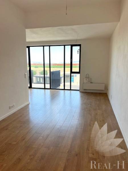 Světlý obývací pokoj s velkými okny a podlahou s dřevěným dekorem v 2-pokojovém bytě.