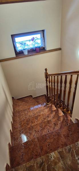 Schodiště v rodinném domě s keramickou dlažbou a dřevěným zábradlím.