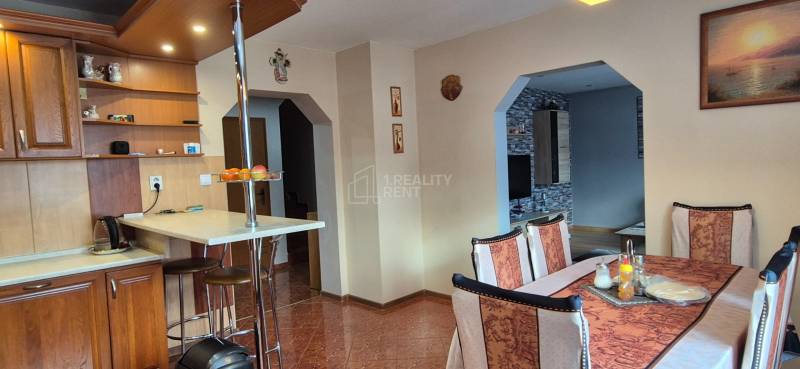 Jídelna v rodinném domě s dřevěnými prvky, stolem a židlemi, světlý interiér.