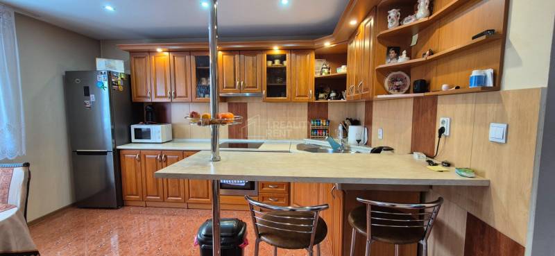 Kuchyně v rodinném domě s dřevěnými skříňkami, barovým pultem a spotřebiči.