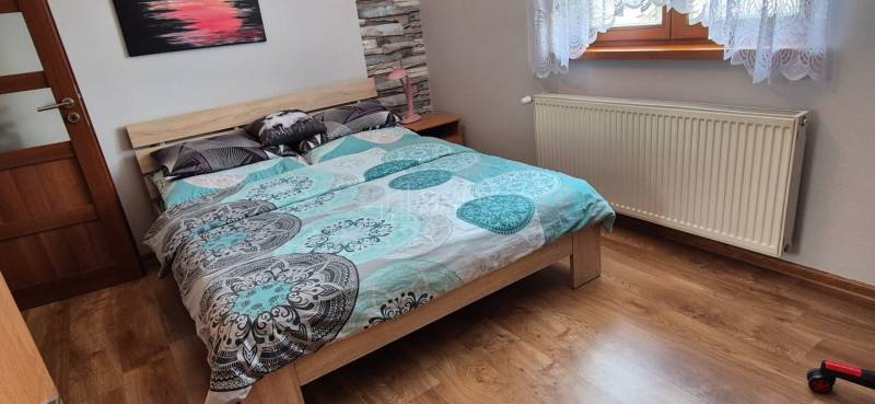 Ložnice v rodinném domě s postelí, radiátorem a podlahou s dřevěným dekorem.