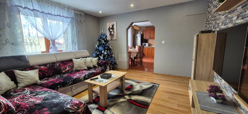 V obývacím pokoji rodinného domu je sedačka, vánoční stromeček a podlaha s dřevěným dekorem.