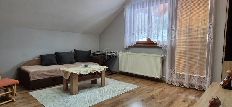 Obývací pokoj v rodinném domě s pohovkou, stolkem, kobercem a podlahou s dřevěným dekorem.