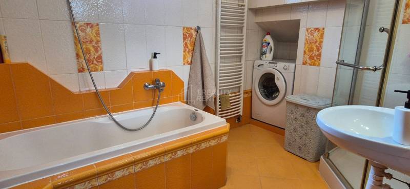 Koupelna v rodinném domě s vanou, umyvadlem, pračkou a žlutou dlažbou.