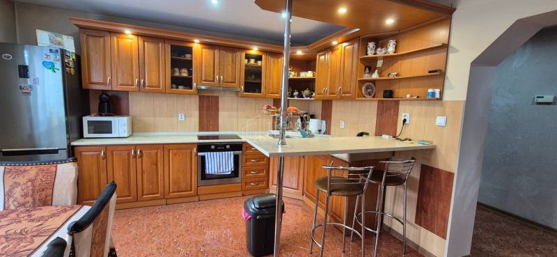 Kuchyně v rodinném domě s dřevěným dekorem, vybavená spotřebiči a barovým pultem.