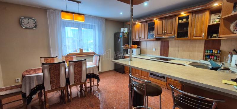 Kuchyně s jídelním stolem v rodinném domě, dřevěné skříňky a podlaha s dlažbou.