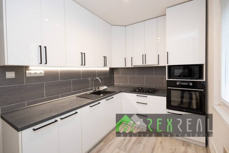 Kuchyně v 3-pokojovém bytě s bílými skříňkami a spotřebiči, podlaha s dřevěným dekorem.