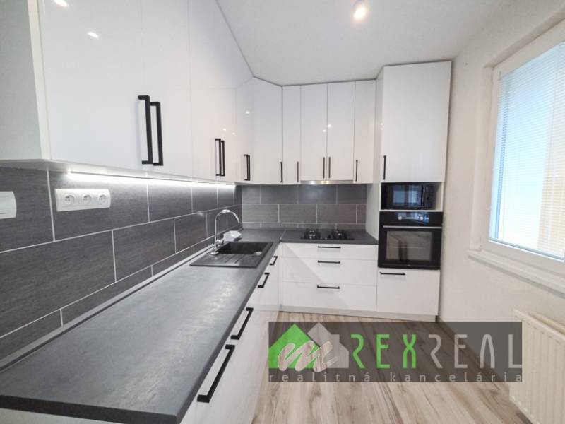 Kuchyně v 3-pokojovém bytě s bílými skříňkami a podlahou s dřevěným dekorem.