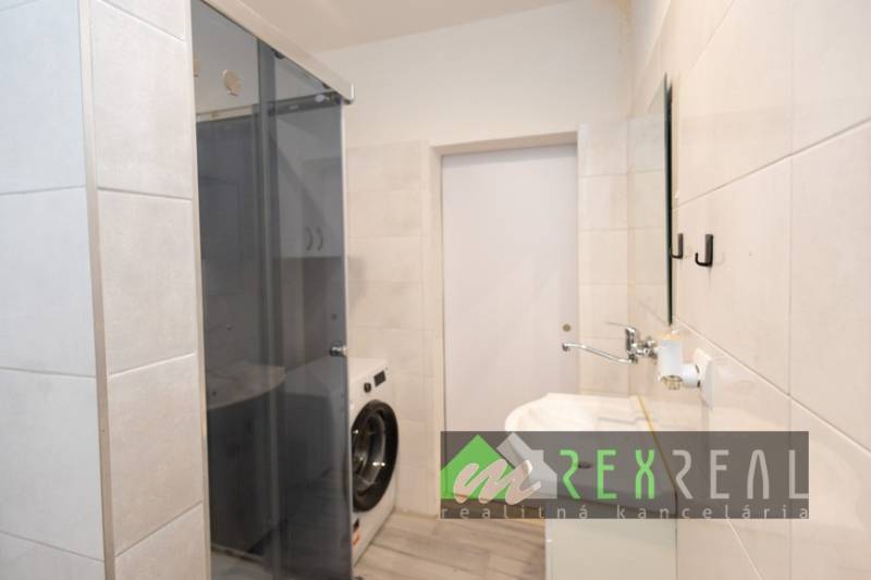 Koupelna ve 3-pokojovém bytě se sprchovým koutem a pračkou, obklady na stěnách.