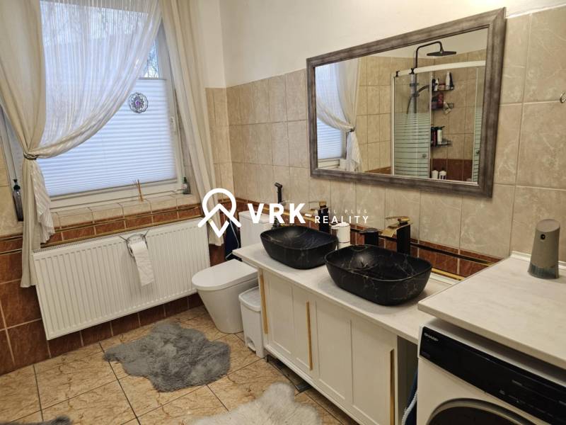 Koupelna v rodinném domě s dvojitým umyvadlem, vanou a pračkou na dlažbě.